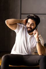 Fototapeta premium Business man sitting indoors on stairs near flower pots with plants and talking on the phone. Portrait of a business man talking on the phone in a cozy room.