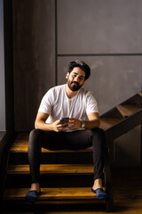 Business man sitting indoors on stairs near flower pots with plants and use phone.