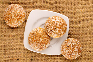 Several sweet tasty gingerbread cookies with white ceramic dishes on jute cloth, macro, top view.