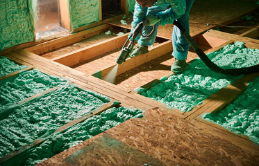 Male builder insulating wooden frame house. Cropped view of man worker spraying polyurethane foam...