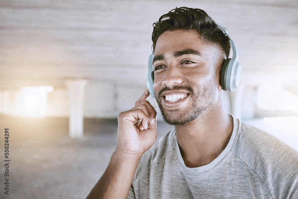 Poster Workout music, fitness headphones or digital radio. Music technology device plays music, smiling relaxed indian man listening to audio sound earphone while exercising in city parking lot closeup.