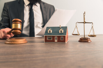 The hand of a judge with a gavel and a model of a house mediating property disputes in court