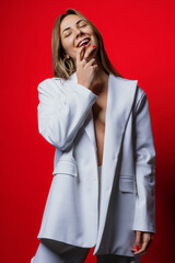 Portrait of a sexy brunette in a light jacket and trousers on a red background. Fashion industry