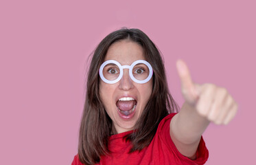 woman red t shirt wow face holding in front finger thumbs up isolated on pink.advertising banner copy paste christmas march 8th women mothers day celebration.female wear wizard round frame glasses