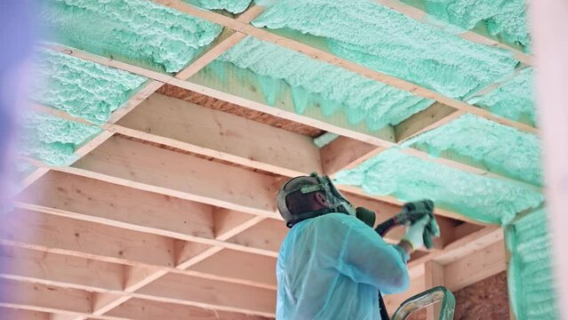 Male builder insulating wooden frame house. Man worker spraying polyurethane foam inside of future cottage, using plural component gun. Construction and insulation concept.