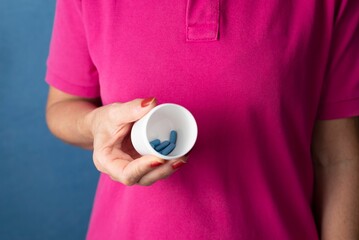 Woman holds a container with blue pills in her hand against a blue background - Medical supplies