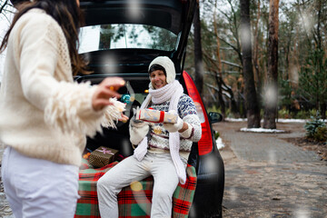 Beautiful young couple giving presents and looking each other sitting in the trunk in winter holidays.