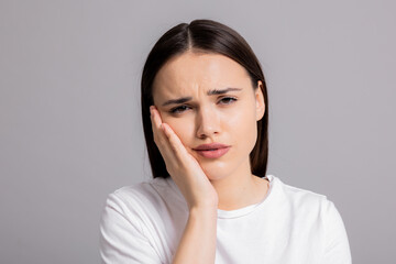 Fototapeta premium Sad woman in white casual t-shirt shows desperate exhausted emotions looking at camera standing on grey background in studio isolated.