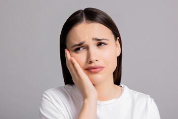 Fototapeta premium Portrait of cried sad young woman wearing white casual t-shirt standing on grey background in studio isolated. Girl suffering from abuse domestic volatile desperate woman.