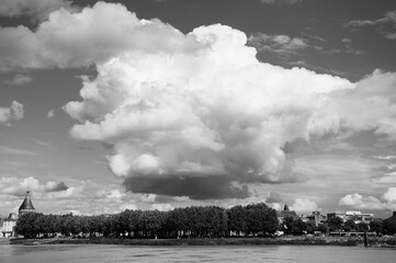Black and white photograph of a bubble shaped cloud hanging above a tree line and a city