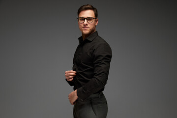Obraz premium Smiling confident young man in black business classic style shirt and grey trousers posing isolated over grey background. Fashion look of businessman. Office style