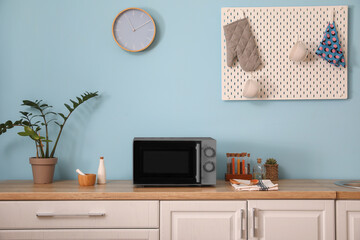 Interior of stylish kitchen with microwave oven near light blue wall - obrazy, fototapety, plakaty