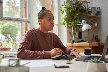 Side view portrait of female artist using graphic tablet with laptop in creative studio