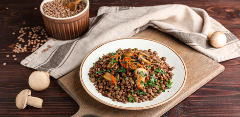 Plate with tasty cooked lentils and mushrooms on wooden table