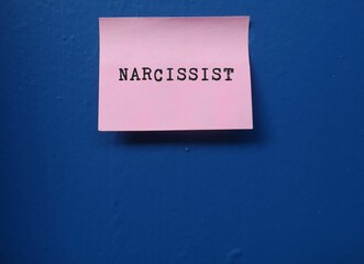 Pink note on blue background with printed text NARCISSIST , self-centered inflated people of...