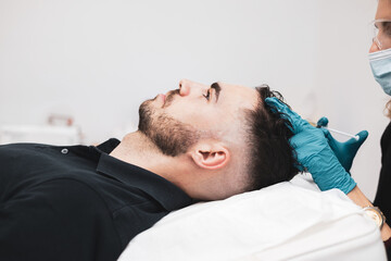 Side view. young man receiving hair treatment in a beauty salon. Man having mesotherapy session in aesthetic clinic, therapist hands in gloves making scalp injection, PRP.