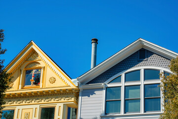 Obraz premium Two colorful houses one beige and purple with visible chimney vents and stucco exterior with windows and front yard trees