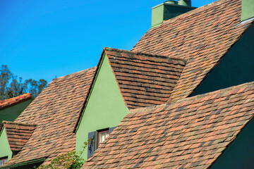 Waves of dark brown roofs with single gable style roof with green stucco exterior and visible shade on side of house or home