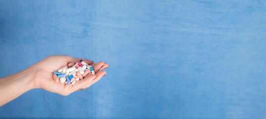 Closeup shot of a person holding a handful of different pills with a blue background