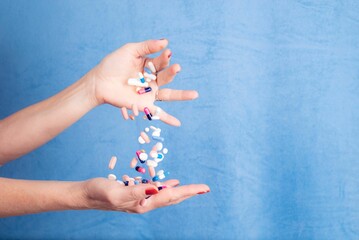Person transferring a handful of different pills from one hand to another on a blue background