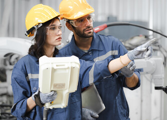 Male industrial engineer using remote control board to check robotic welder operation in modern...