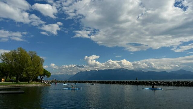 Rowing team on water. Landscape of Lake Geneva, tree, sky and clouds. Time lapse. Lausanne, Vaud Canton, Switzerland.