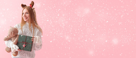 Young woman with Christmas present, toy and falling snow on pink background with space for text