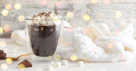 Cup of hot chocolate with marshmallows and warm sweater on white table