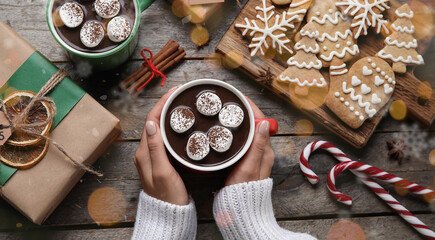 Hands with cup of hot chocolate, Christmas gift and cookies on wooden background