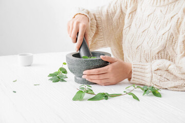 Woman grinding herbs in mortar on white wooden table - obrazy, fototapety, plakaty