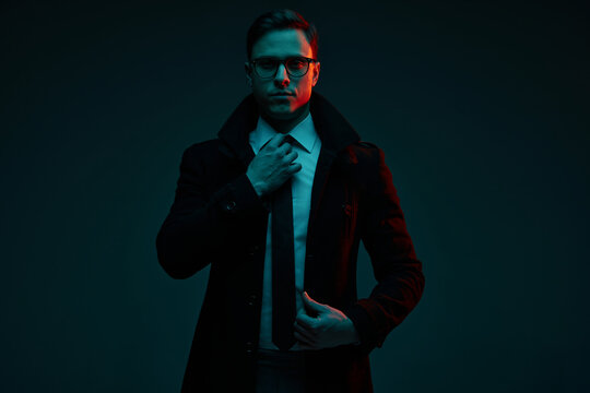 Studio Shot Of Serious Young 30s Years Old Man In Classic Style Clothes Posing Isolated Over Dark Background In Neon Light. Fashion, Style, Emotions Concept