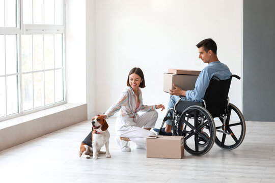 Young woman with dog and her husband in wheelchair in their new flat on moving day