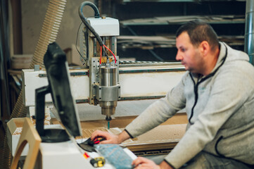 Factory worker operating drilling cnc machine at wood machining industry