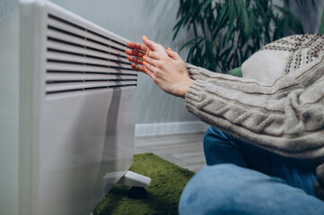 Close-up of hands at the heater. The woman reaches out with her hands to the heat of the radiator.