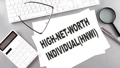 HNWI high net worth individuals text on paper with keyboard, calculator on grey background