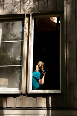 A woman sits at an open window in a wooden house and hugs her mongrel dog