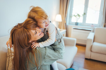 Lovely mother embracing her cute daughter on the sofa at home. Lovely Family. Mother embracing her...