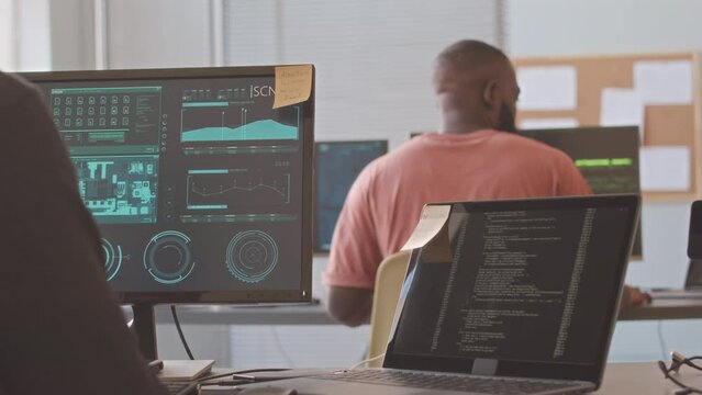 Back view of concentrated software developers coding and examining pcb design software while working by computers at contemporary office