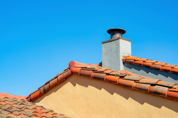 Orange building exterior with adobe red roof tiles and white stone chimney with metal vent and...