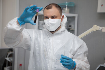 Fototapeta premium Scientific virologist. Biologist in protective suit and blue gloves holds test tube with blood. Test tube with viruses concept. Virus University employee.