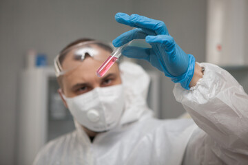 Scientific virologist. Biologist in protective suit and blue gloves holds test tube. Test tube with viruses concept. Medicine and antidote in doctor hands. Virus University employee.