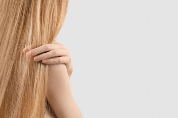 Woman touching blonde hair on light background