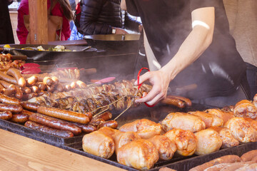 A man on the street fried on a large grill a lot of different meats and sausages during the street...