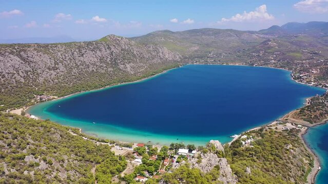 Aerial drone video of scenic lake Vouliagmeni in Corinthia near famous lighthouse of Heraion and city of Loutraki featuring crystal clear turquoise beach and calm waters, Perachora, Greece