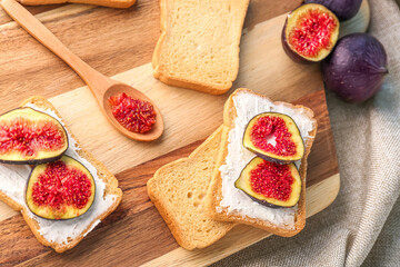 Wooden board of tasty bruschettas with cream cheese and fresh figs on table, closeup
