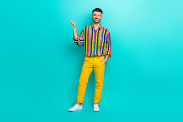 Full length photo of young satisfied smiling guy wear striped colorful shirt finger direct empty space useful tips isolated on cyan color background