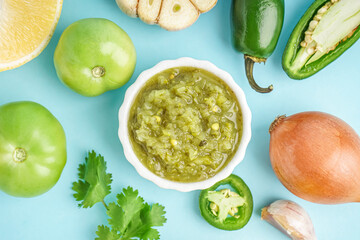 Bowl of tasty green salsa sauce with ingredients on color background