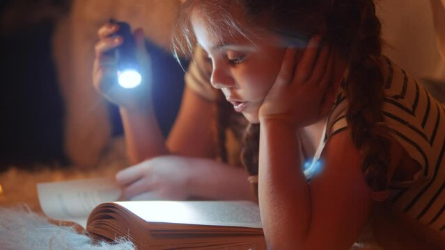 stay home. children in a wigwam tent play at night with a flashlight and read a book. happy family kid dream concept. children reading book with a flashlight. kid dream reading a book in a tent house