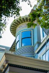 Spire or turret with decorative facade and wooden pannels with foreground roof edge and front yard trees in the neighborhood shade