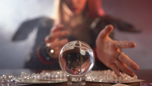 Occult witch performing spelling rituals with person's photos using round crystal mystery ball, scary scene of potion cult in dark illuminated room, witchcraft and afterlife concept